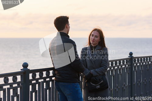 Image of Girl anxiously looks at a guy near a railing in the background of the sea in cloudy weather