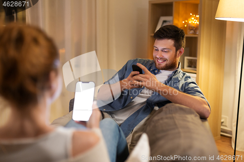 Image of couple with smartphones at home in evening