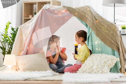 Image of girls playing with torch in kids tent at home