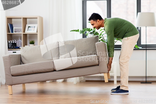 Image of happy indian man moving sofa at home