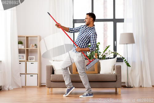 Image of man with broom cleaning and having fun at home