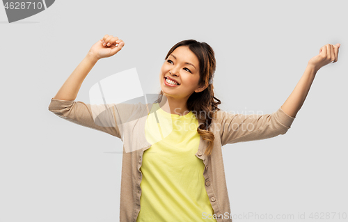 Image of happy asian woman dancing over grey background
