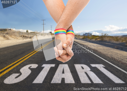 Image of hands of couple with gay pride rainbow wristbands