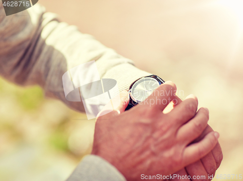 Image of senior man checking time on wristwatch outdoors