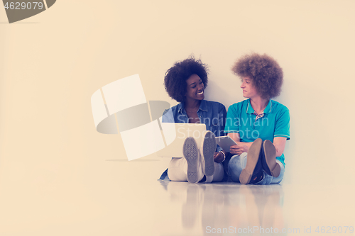 Image of multiethnic couple sitting on the floor with a laptop and tablet