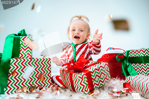 Image of Cute baby girl 1 year old near santa hat posing over Christmas background. Sitting on floor with Christmas ball. Holiday season.