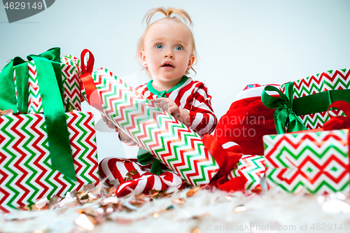 Image of Cute baby girl 1 year old near santa hat posing over Christmas background. Sitting on floor with Christmas ball. Holiday season.