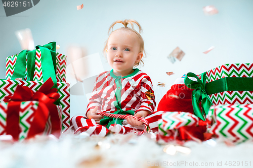 Image of Cute baby girl 1 year old near santa hat posing over Christmas background. Sitting on floor with Christmas ball. Holiday season.