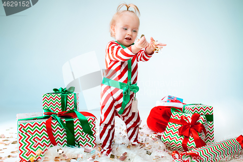 Image of Cute baby girl 1 year old wearing santa hat posing over Christmas background. Sitting on floor with Christmas ball. Holiday season.