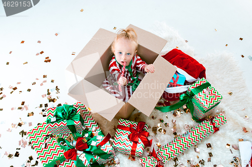 Image of Cute baby girl 1 year old sitting at box over Christmas background. Holiday season.