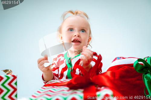 Image of Cute baby girl 1 year old near santa hat posing over Christmas background. Sitting on floor with Christmas ball. Holiday season.