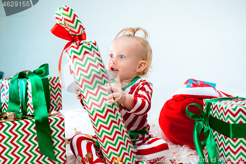 Image of Cute baby girl 1 year old near santa hat posing over Christmas background. Sitting on floor with Christmas ball. Holiday season.