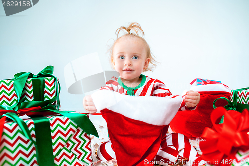 Image of Cute baby girl 1 year old wearing santa hat posing over Christmas background. Sitting on floor with Christmas ball. Holiday season.