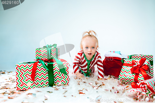 Image of Cute baby girl 1 year old near santa hat posing over Christmas background. Sitting on floor with Christmas ball. Holiday season.