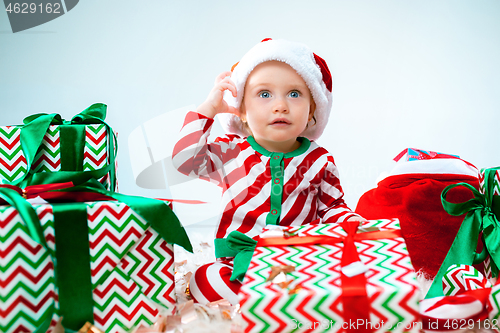 Image of Cute baby girl 1 year old wearing santa hat posing over Christmas background. Sitting on floor with Christmas ball. Holiday season.