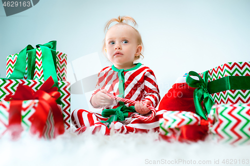 Image of Cute baby girl 1 year old near santa hat posing over Christmas background. Sitting on floor with Christmas ball. Holiday season.