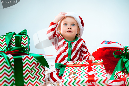 Image of Cute baby girl 1 year old wearing santa hat posing over Christmas background. Sitting on floor with Christmas ball. Holiday season.