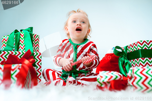 Image of Cute baby girl 1 year old near santa hat posing over Christmas background. Sitting on floor with Christmas ball. Holiday season.