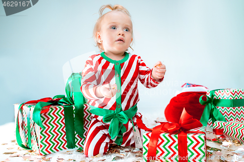 Image of Cute baby girl 1 year old near santa hat posing over Christmas background. Sitting on floor with Christmas ball. Holiday season.