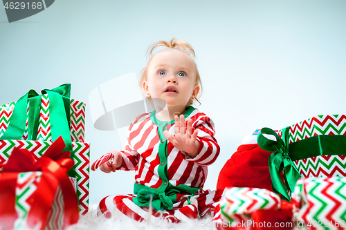 Image of Cute baby girl 1 year old near santa hat posing over Christmas background. Sitting on floor with Christmas ball. Holiday season.