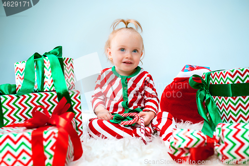 Image of Cute baby girl 1 year old near santa hat posing over Christmas background. Sitting on floor with Christmas ball. Holiday season.