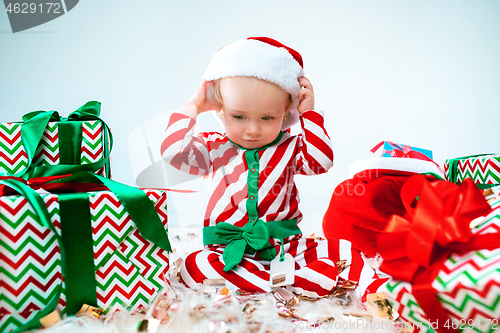 Image of Cute baby girl 1 year old wearing santa hat posing over Christmas background. Sitting on floor with Christmas ball. Holiday season.