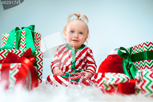 Image of Cute baby girl 1 year old near santa hat posing over Christmas background. Sitting on floor with Christmas ball. Holiday season.