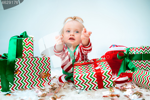 Image of Cute baby girl 1 year old near santa hat posing over Christmas background. Sitting on floor with Christmas ball. Holiday season.