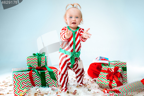 Image of Cute baby girl 1 year old wearing santa hat posing over Christmas background. Sitting on floor with Christmas ball. Holiday season.