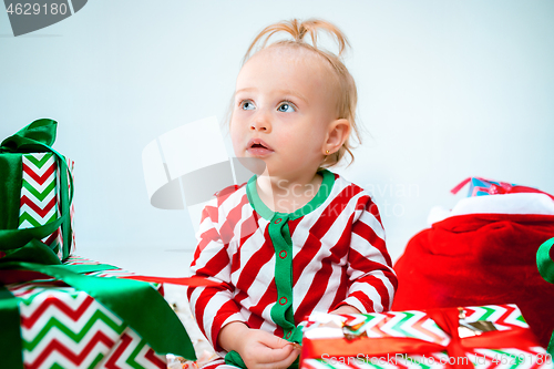 Image of Cute baby girl 1 year old near santa hat posing over Christmas background. Sitting on floor with Christmas ball. Holiday season.