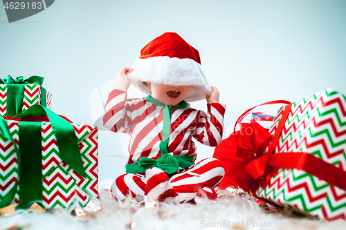 Image of Cute baby girl 1 year old wearing santa hat posing over Christmas background. Sitting on floor with Christmas ball. Holiday season.