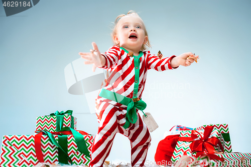 Image of Cute baby girl 1 year old wearing santa hat posing over Christmas background. Sitting on floor with Christmas ball. Holiday season.