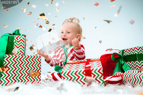 Image of Cute baby girl 1 year old near santa hat posing over Christmas background. Sitting on floor with Christmas ball. Holiday season.