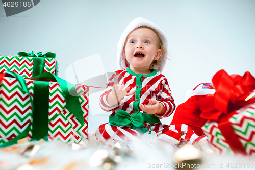 Image of Cute baby girl 1 year old wearing santa hat posing over Christmas background. Sitting on floor with Christmas ball. Holiday season.