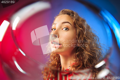 Image of The surprised young woman in party clothes posing with glass of wine.