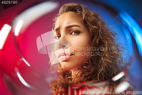 Image of The surprised young woman in party clothes posing with glass of wine.