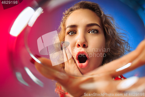 Image of The surprised young woman in party clothes posing with glass of wine.