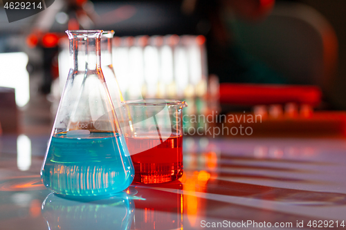 Image of Illuminated laboratory flask filed with colorful chemical solutions with shadows on the table. Laboratory, science, chemistry... consept.