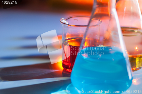 Image of Illuminated laboratory flask filed with colorful chemical solutions with shadows on the table. Laboratory, science, chemistry... consept.