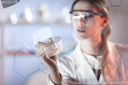 Image of Portrait of a confident female researcher in life science laboratory writing structural chemical formula on a glass board.