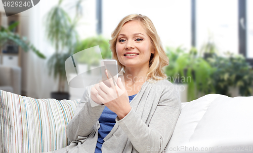 Image of smiling woman with smartphone texting at home