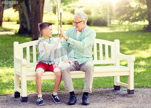 Image of old man and boy making high five at summer park