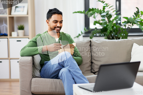 Image of indian man with laptop eating takeout food at home