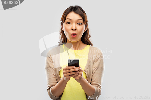 Image of surprised asian woman using smartphone