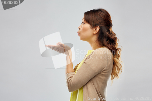 Image of asian woman holding something on hand and blowing