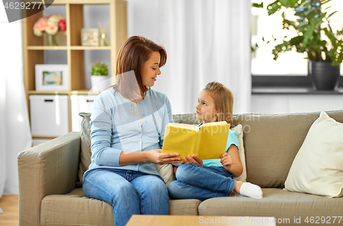 Image of happy girl with mother reading book at home