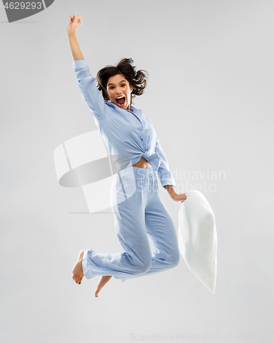 Image of happy woman in blue pajama jumping with pillow