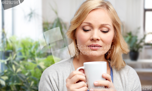 Image of smiling woman with cup of tea or coffee at home