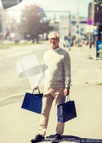 Image of senior man with shopping bags walking in city