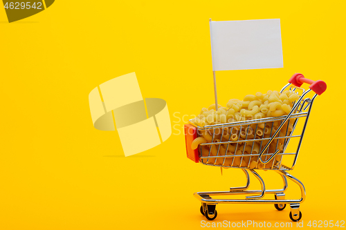 Image of The grocery cart is filled with pasta on a bright orange background, a flag is stuck in the basket